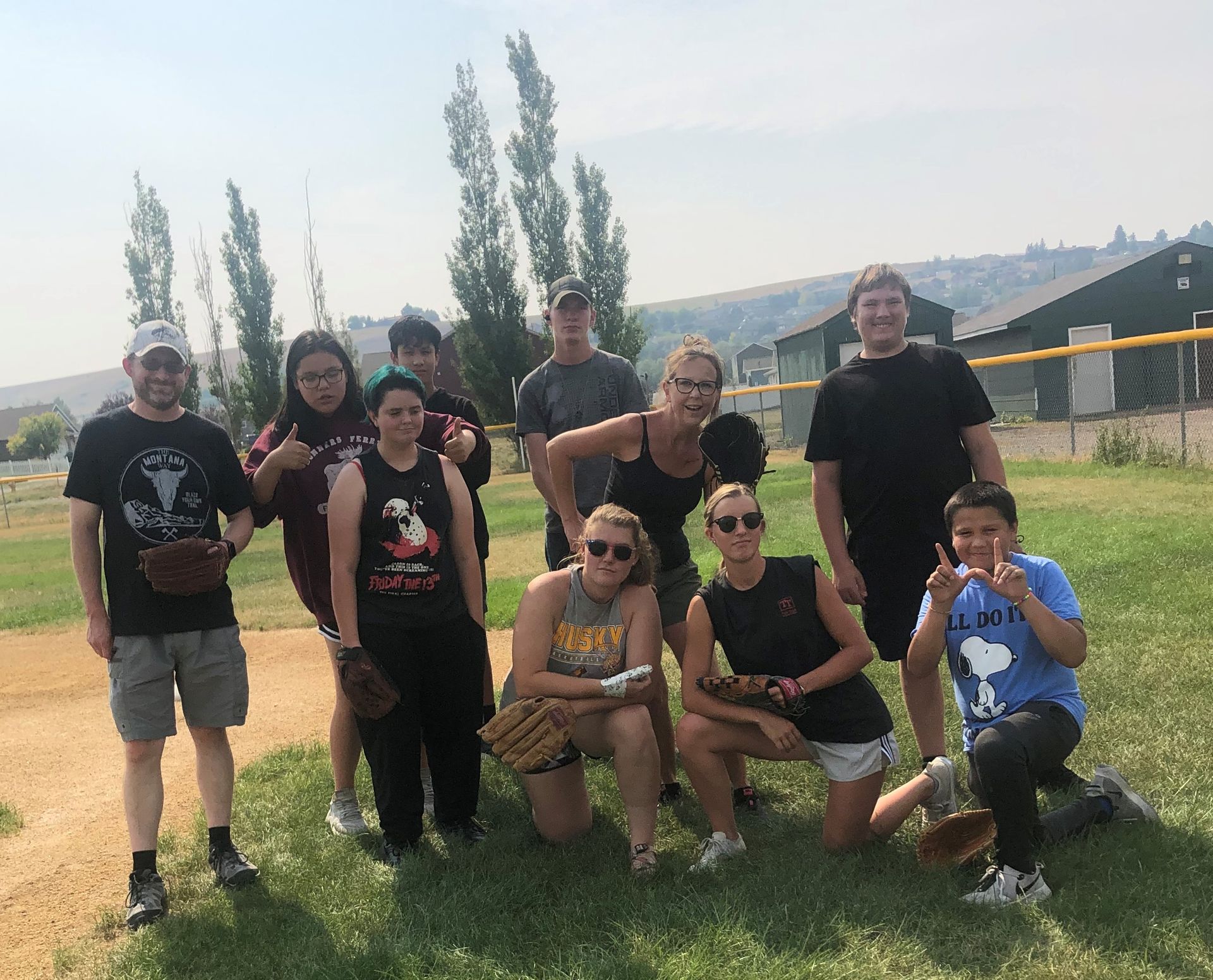 Young adults wearing baseball gloves posing for a photo on a baseball field.